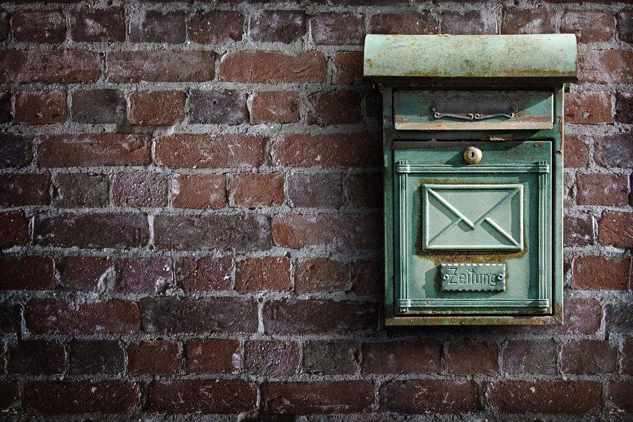 Boîte aux lettres verte sur un mur de briques