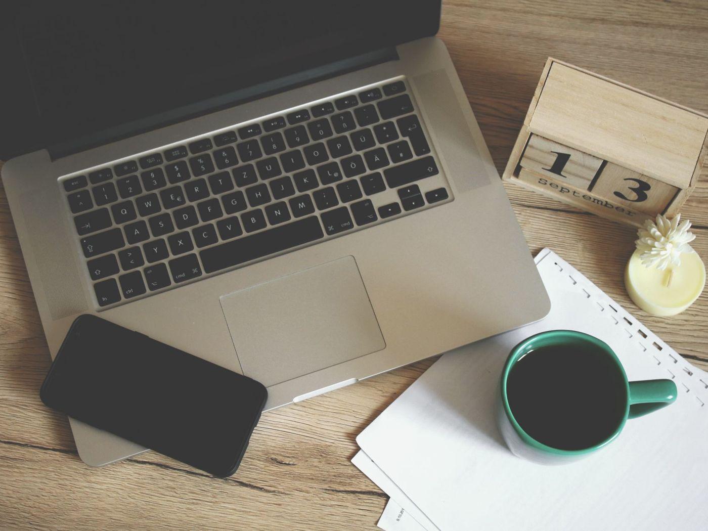 Laptop, Smartphone, Kaffeetasse und Tischkalender auf einem Holztisch